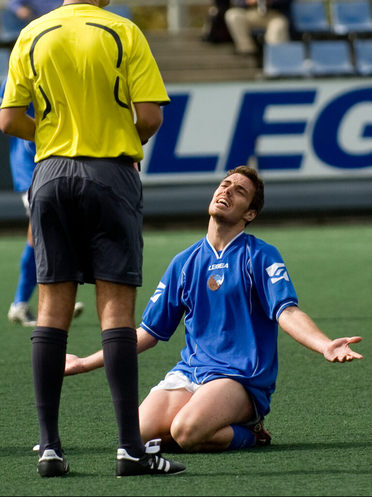 jugador de fútbol recibe una tarjeta amarilla desde el suelo con los brazos cruzados
